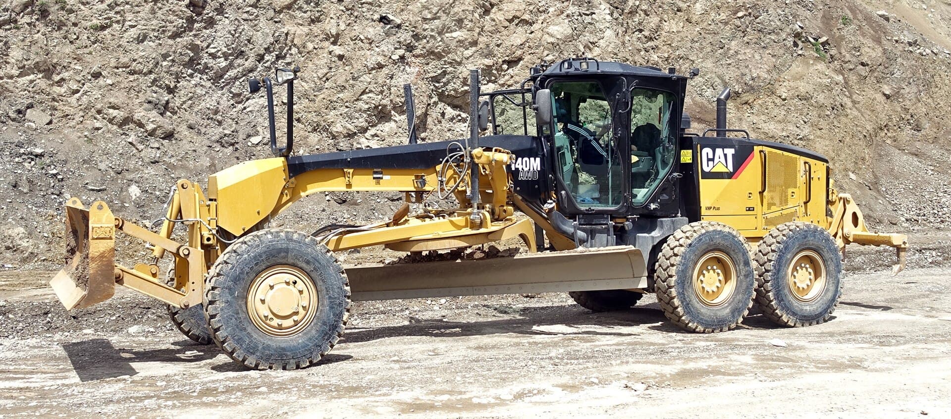 Motor grader finishing a mine haul road against a rock face