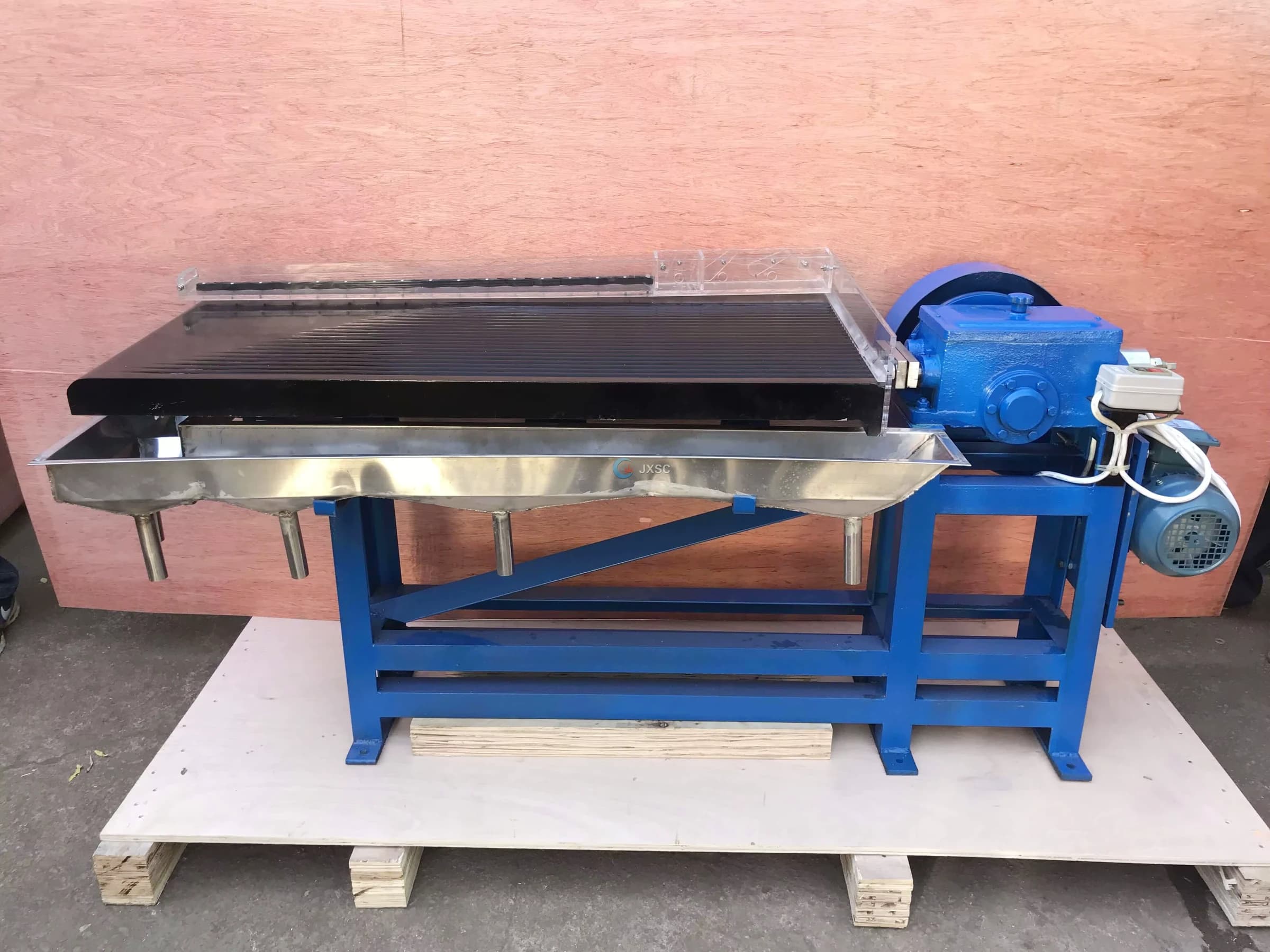 A gold shaking table separates heavy particles on a moving deck using water flow and gravity.